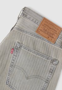 Poche arrière grise claire de jeans Levi's avec tissu à motif chevron, étiquette rouge Levi's et label en cuir fauve Levi Strauss & Co. à la ceinture.