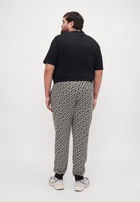 Top negro de manga corta con cuello y acento en tres colores; pantalones de chándal de patrón en blanco y negro con puños elásticos; zapatillas grises con suelas blancas.