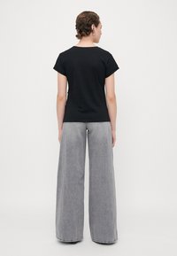 Svart t-shirt med kort ärm, tillsammans med högmidjade, vida grå jeans. Tyget ser mjukt ut, med en subtil textur och en avslappnad passform.