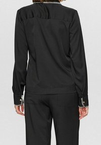 Black long-sleeve blouse with a smooth texture, featuring decorative stitching along the collar and cuffs. Slightly loose fit.