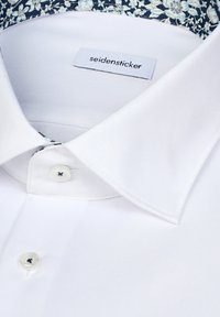 Weißes Hemd mit spitzem Kragen und floralem Innenfutter, ausgestattet mit zwei weißen Knöpfen und einem "seidensticker" Markenzeichen innen am Kragen.
