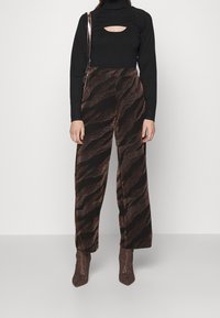 Un col roulé noir avec une découpe en forme de trou de clé, associé à un pantalon large marron avec un motif texturé en vagues, porté avec des bottes à talons assorties.