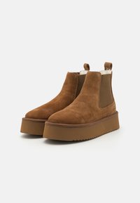 Brune suedes ankelstøvler med elastiske sidepaneler, rund tå og tyk gummiplatformssål med rillet tekstur for greb.
