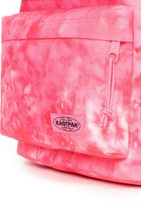 Rosa tie-dye tyg framförficka på en Eastpak-ryggsäck med dragkedja och en märkesetikett i nedre mitten av fickan.