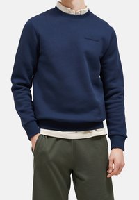 Sudadera color azul marino de un tejido suave, con cuello redondo y puños acanalados, que presenta un sutil logo bordado en el pecho.