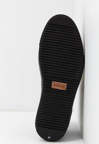 Semelle de chaussure noire avec des rainures horizontales, une étiquette marron « Blackstone » et la taille 37 sur fond blanc.