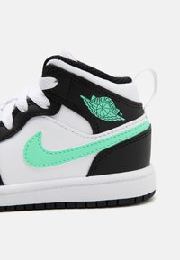 Černobílé tenisky s mátově zelenými akcenty, kožený svršek, polstrovaný límec a gumová podrážka se strukturovaným vzorkem. Přítomné logo Air Jordan.