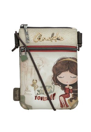 Bolso bandolera pequeño de color crema con una niña de dibujos animados con vestido rojo, logo "Anekke", texto "Conócete a ti mismo" y un charm de gato en la cremallera frontal.
