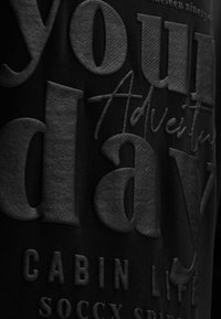 Close-up of textured black fabric with embossed large letters and cursive text reading "Your Adventure."
