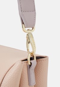 Skórzana torba o usztywnionej formie, wykonana z miękkiej, jasnobeżowej skóry. Posiada lawendowy pasek i złotą klamrę z detalem pod marką.