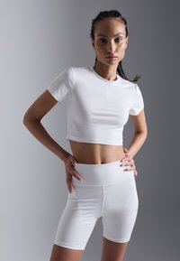 Hvit, kort atletisk t-skjorte og høy midje shorts, begge laget av glatt, elastisk stoff. Fitted design med enkle linjer og ingen mønstre.