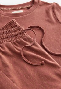 Ein rostfarbener Oberteil und passende, elastische Shorts mit einem gepunkteten Muster in Olivgrün. Weicher Stoff mit verstellbarem Kordelzugdetail an den Shorts.