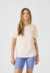 Camiseta beige claro hecha de algodón suave con cuello redondo y mangas cortas, combinada con pantalones cortos de ciclismo de lavanda con canalé.