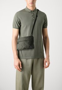 Borsa a tracolla verde oliva realizzata in nylon matelassé morbido, con una tasca con zip e un patch logo nero. Cinghia regolabile inclusa.