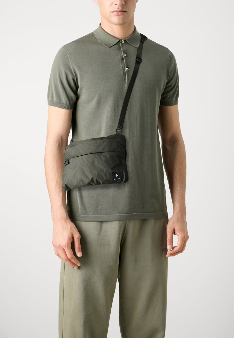 Borsa a tracolla verde oliva realizzata in nylon matelassé morbido, con una tasca con zip e un patch logo nero. Cinghia regolabile inclusa.