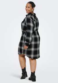 Black and gray plaid dress with long sleeves, featuring a belted waist and a relaxed fit. Worn with black ankle boots.
