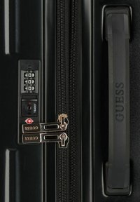 Valigia nera con lucchetto a combinazione, doppie cerniere con accenti dorati, superficie testurizzata e maniglia laterale con il marchio "GUESS."