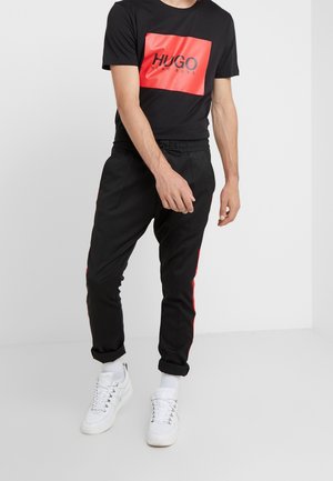 Black T-shirt with red rectangular logo; black joggers with red side stripes; white sneakers; smooth fabric; relaxed fit; no patterns.