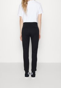 Pantalons noirs fuselés avec une texture lisse, deux poches arrière et une taille mi-haute associés à un t-shirt blanc uni et des sneakers sombres.
