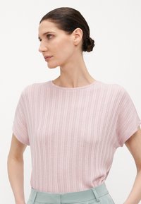 Top de punto rosa claro con rayas horizontales, mangas cortas y escote redondeado, combinado con pantalones sastre verde claro.