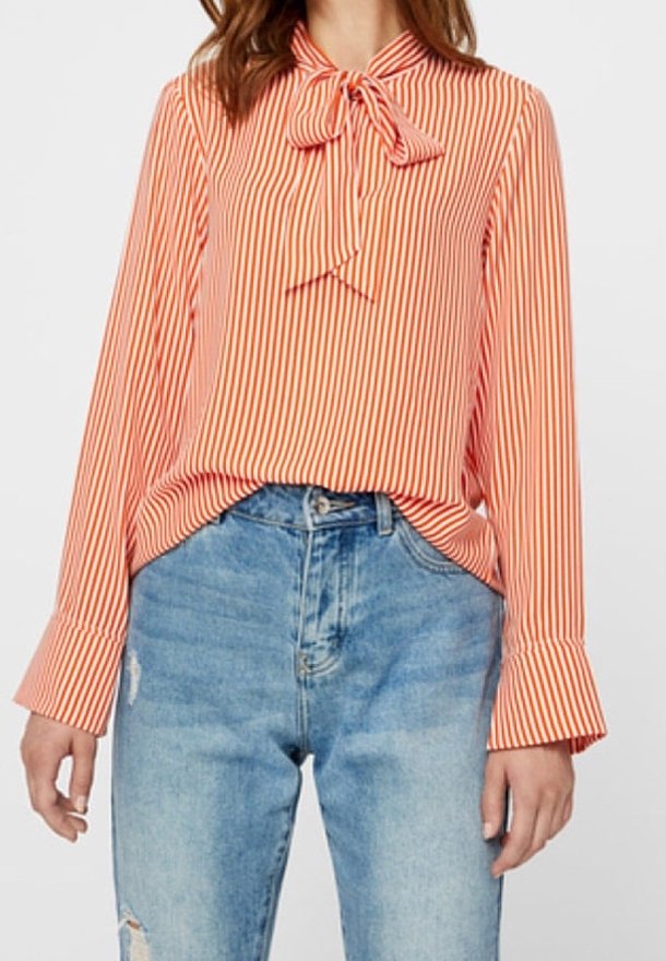 Femme portant un chemisier à rayures verticales orange et blanc avec un col noué en nœud papillon et un jean bleu taille haute déchiré.