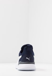 Granatowy sportowy but z materiałową cholewką, białym logo i szarą podeszwą. Posiada pętlę do ściągania na pięcie oraz teksturowane akcenty.