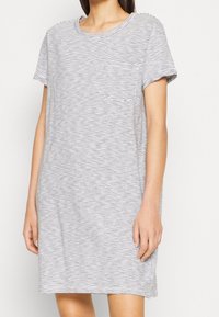 Randig t-shirtklänning i grått och vitt, kort ärm, rund halsringning, framficka, avslappnad passform och sprund på sidorna vid fållen.