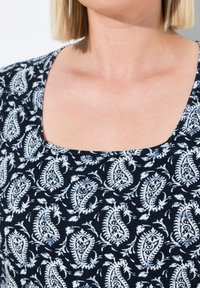 Top azul marino con escote cuadrado, que presenta un estampado de cachemira blanco y acentos florales. La tela tiene una textura suave y lisa.