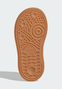 Semelle en caoutchouc marron avec un motif de traction texturé, des accents circulaires et le logo Adidas. Présente une bordure ondulée et des détails en relief.