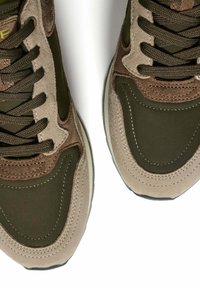 Par de zapatillas marrones y verde oliva con paneles de ante y tela, cordones marrones oscuros y costuras texturizadas sobre un fondo blanco.