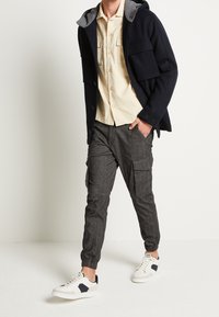 Marineblauwe hoodie met grijze voering, crèmekleurig shirt met korte mouwen, donkergrijze cargobroek en witte sneakers met marineblauwe accenten.