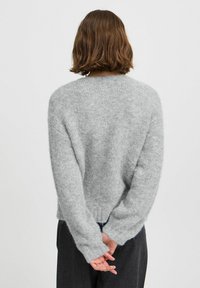 Pull léger gris clair, moelleux, avec un col rond et des manches longues. Présente une coupe légèrement ample et un ourlet côtelé, vu de dos.