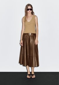 Khaki knitted top with a floral detail, paired with a brown leather A-line skirt. Accessories include dark sunglasses and simple sandals.