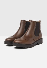 Bottines en cuir marron avec panneaux élastiques sur les côtés, détails brogue au niveau des orteils et une semelle en caoutchouc noir robuste. Conception à talon plat.