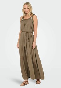 Robe maxi en vert olive, fabriquée en tissu léger, dotée de plis, d'une taille nouée et de bretelles tressées. Associée à des sandales plates marron.