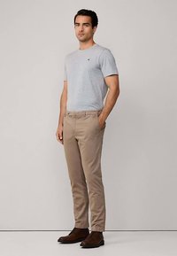 Szara bawełniana koszulka z okrągłym dekoltem, beżowe wąskie chinosy i brązowe skórzane buty, stojące na neutralnym tle.