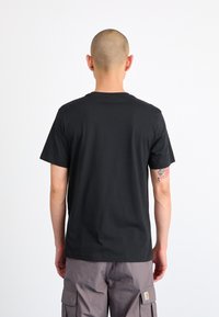 Svart bomulls-t-skjorte med rund hals og korte ermer, sett fra baksiden. Har en jevn tekstur og minimalistisk design, uten grafikk.