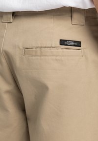 Pantaloni khaki beige realizzati in misto cotone, caratterizzati da una tasca posteriore con un'etichetta nera che recita "Element Skateboard Co." e una vita standard.