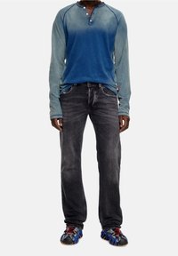 Blue long-sleeve henley shirt with a gradient design, dark gray jeans, and black and blue sporty shoes with red accents.
