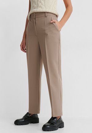 Pantalones beige de talle alto y pierna recta, combinados con mocasines negros gruesos y una camiseta de punto crema sin mangas.