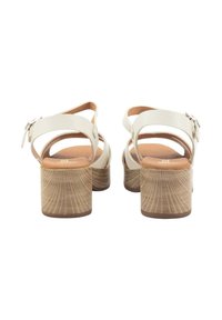 Sandalias de tacón blanco con correas texturizadas, hebilla ajustable en el tobillo y un tacón bloque marrón con un patrón radial. Plantillas suaves y acolchadas.