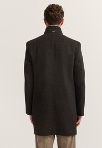 Czarny długi płaszcz z wysokim kołnierzem, dopasowany krój, teksturowany materiał oraz szew wzdłuż środka pleców; posiada małe logo na karku.