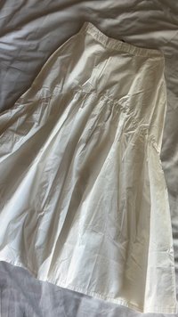 Saia branca até aos tornozelos, feita de um tecido leve com uma cintura franzida e um design fluido e plissado. Textura suave com mínimas rugas.