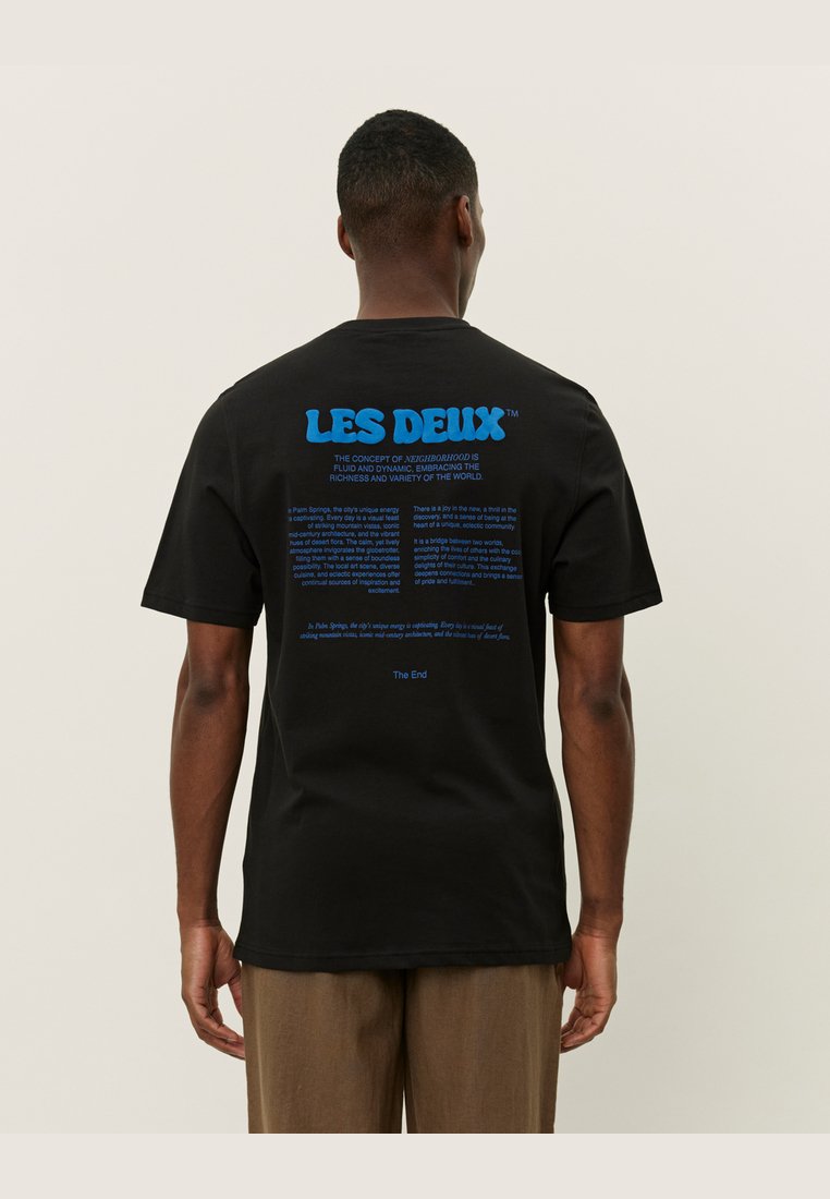 Svart bomull t-skjorte med en blå grafisk tekstdesign på baksiden, med merkenavnet "LES DEUX" og tilleggstekst under.