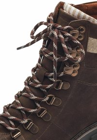 Botte de randonnée en cuir marron avec surface texturée, doublure à carreaux contrastante et lacets marron à motifs maintenus par des crochets métalliques.