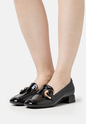 Mocassins en cuir verni noir avec un petit talon bloc, ornés d'une boucle décorative dorée et de détails de couture le long des bords.