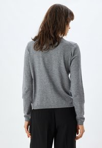 Suéter gris hecho de una tela suave, con mangas largas, cuello redondo y dobladillo acanalado. La vista desde atrás muestra una textura suave y un diseño sencillo.