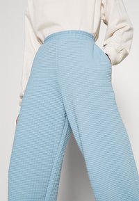 Hellblaue Textilhosen mit einem Karomuster, im weit geschnittenen Design und mit elastischem Bund, ausgestattet mit Seitentaschen für zusätzliche Funktionalität.