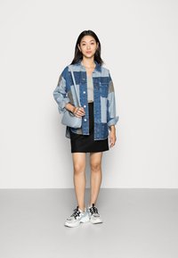 Jeans jakna z barvitimi nalepkami, siva kratka majica, črna mini krila in bele superge z modrimi detajli. Srebrna torbica za čez telo.