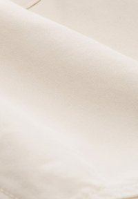 Béžová tkanina, hladký povrch, mírně lesklý, viditelné záhyby a vrásky, žádné vzory nebo akcenty. Měkký a flexibilní materiál.